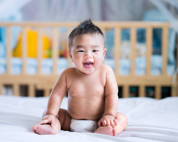 istock Asian new born baby sit and smile on a white bed 953047584
