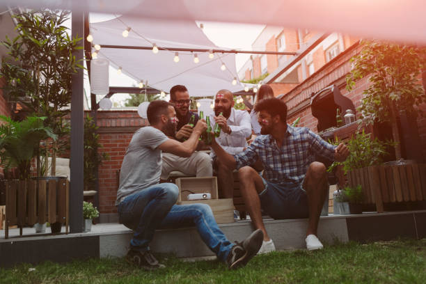 Friends watching soccer game on big screen in backyard. Cheering and drinking beer.