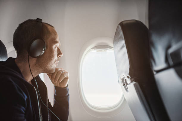 Traveling man on airplane flying Traveling man on airplane flying charter. 
Using smartphone and using noise-cancelling headphones window seat vehicle stock pictures, royalty-free photos & images