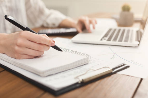 primer plano de mujer las manos escribiendo en el portátil y contando con calculadora - palmtop fotografías e imágenes de stock