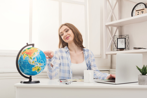 Young pensive woman dreaming about traveling around world, looking at globe at home. Pretty girl studying globe and choosing route of vacation trip, copy space