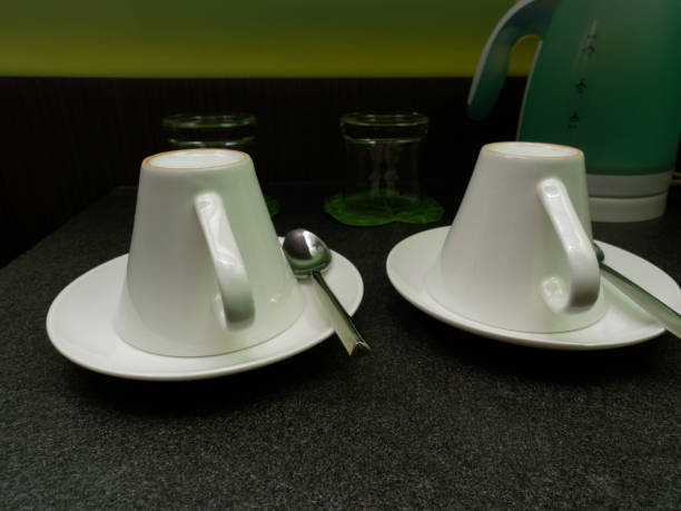 istock Two white coffee cups and tea spoons put upside down with water glasses and kettle in the background 953083168