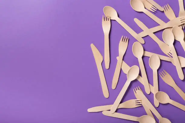Top view on many bamboo spoons and forks on violet background, copy space. Disposable take away table wear concept