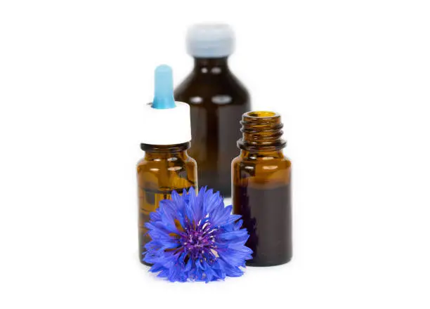herbal essential oil in glass bottles with blue organic flower isolated on white background