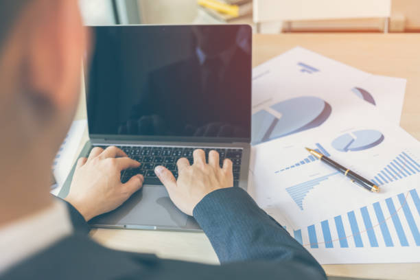 istock Close up modern businessman typing laptop or notebook with chart paper in business documents of graph financial diagram on table. Business success, Report, Growth, Marketing plan, Investment. 953090590