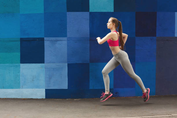 istock Side view of woman running against bright wall 953092346