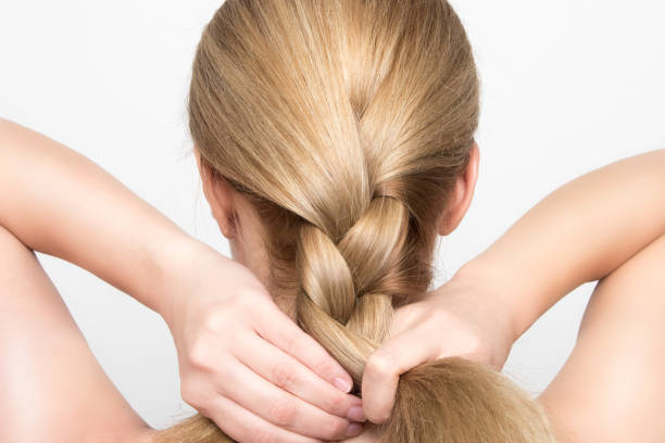 Gorgeous blonde woman braids her hair from behind stock photo