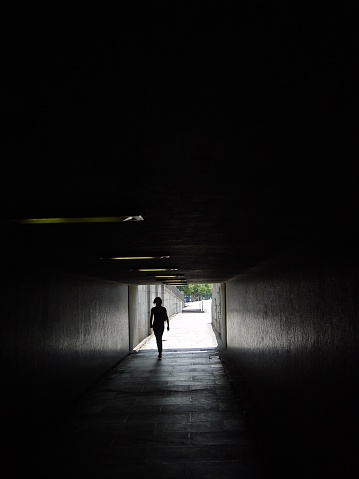Silhouette of a woman stepping into dark underpass.