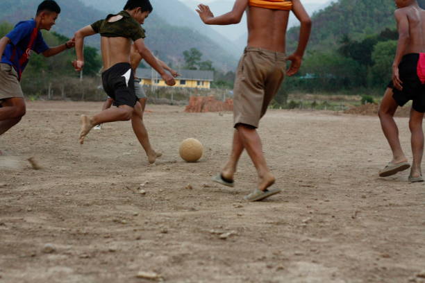 メーホンソン、タイ北部、東南アジア、2018 年 4 月 29 日でサッカー、ほこり汚れフィールドでフットボールの試合は、夜の時間を演奏 10 代と若いタイ ヤイ男の子のチーム - soccer field dirty soccer outdoors ストックフォトと画像