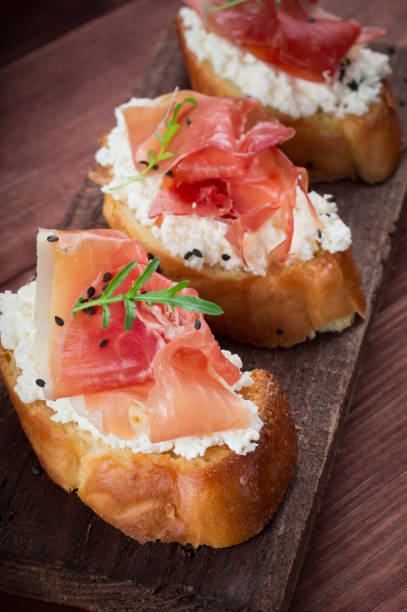 istock Baguette with cottage cheese, arugula and ham, sandwich on a board, selective focus. Wooden rustic background. Top view 953134898