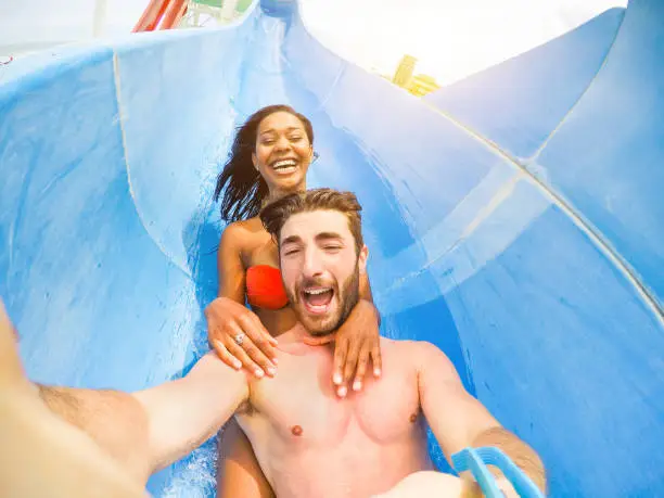 Photo of Young happy friends having fun in aqua park pipe - Cheerful multi race couple taking selfie photo with funny faces - Vacation and love concept - Soft focus on man face - Warm filter