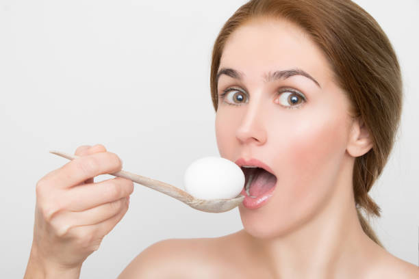 Gorgeous blond woman trying to eat a whole egg with a wooden spoon stock photo