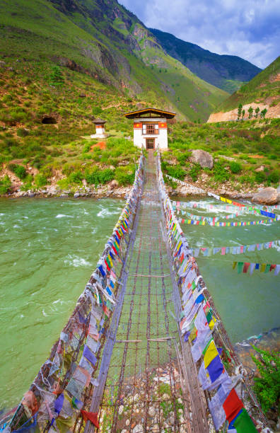 marche de pont suspendu au-dessus de la rivière avec des drapeaux de prière coloré au bhoutan - bhutanese flag photos et images de collection