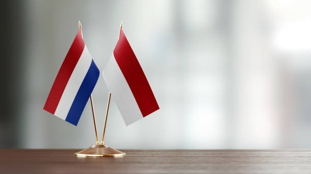 Dutch And Indonesian Flag Pair On A Desk Over Defocused Background