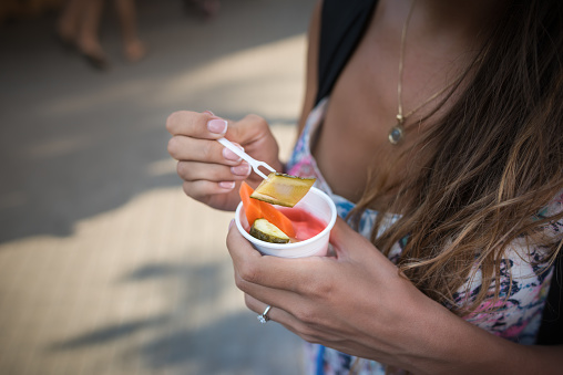 Close-up view of street local food in hands of young woman on blurred background.