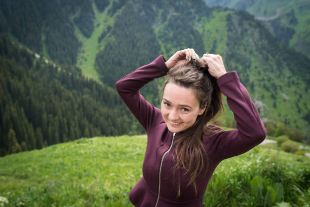 Young woman stands in national park on background of green mountains, hills and forest in summer day.