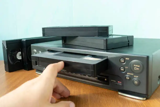 VHS videocassette is put into the video recorder to watch the video, another video cassette is on the video-tape recorder