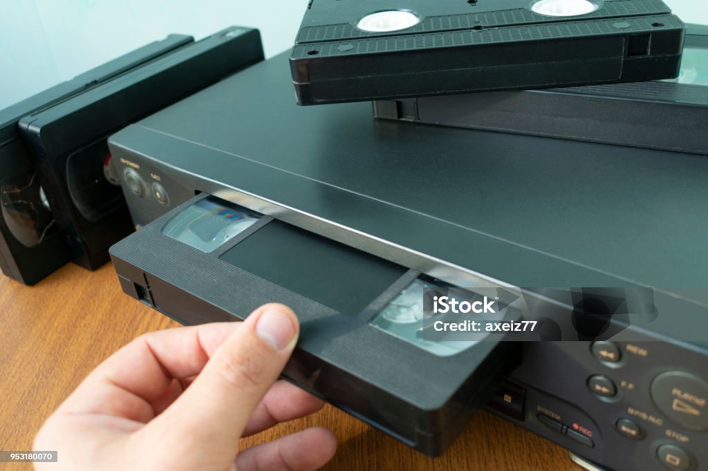 insert a videotape into a tape recorder VHS videocassette is put into the video recorder to watch the video, another video cassette is on the video-tape recorder Videocassette Stock Photo
