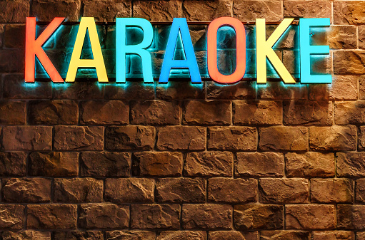 Colorful neon illuminated Karaoke sign on stone building wall background at Rosa Khutor resort. Architectural decor of entertainment facilities