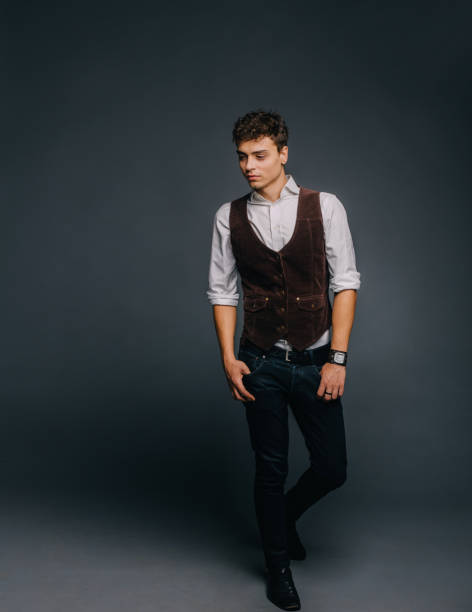 istock A young, handsome guy posing on a gray studio background. The man is stylish and elegantly dressed in jeans, a shirt and a brown vest. 953189464