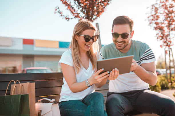 Young couple after finished shopping is sitting on bench outside and enjoying their free time stock photo
