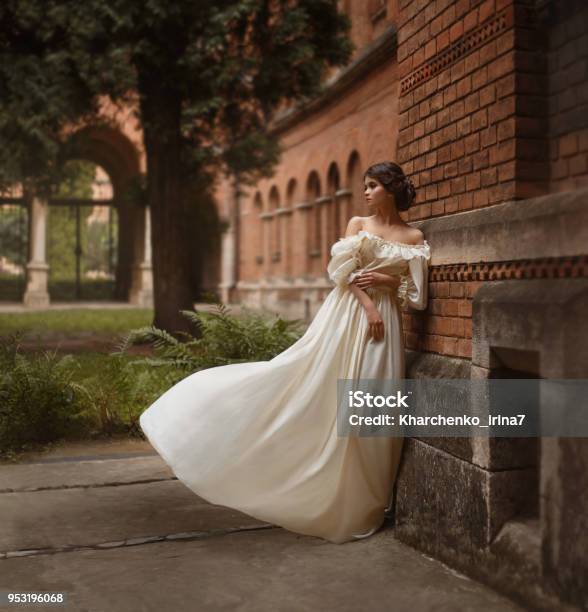 A Young Lady Stands At The Wall Of An Ancient Castle Looking With Hope In The Distance Emotion Waiting For The Longawaited A White Vintage Dress Flutters In The Wind Artistic Photography Stock Photo - Download Image Now