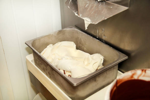 istock Ice cream making machine produces vanilla ice cream with chocolate dressing and it falls into steel container. Industrial preparation of creamy ice cream. Dessert, sweets. 953198024