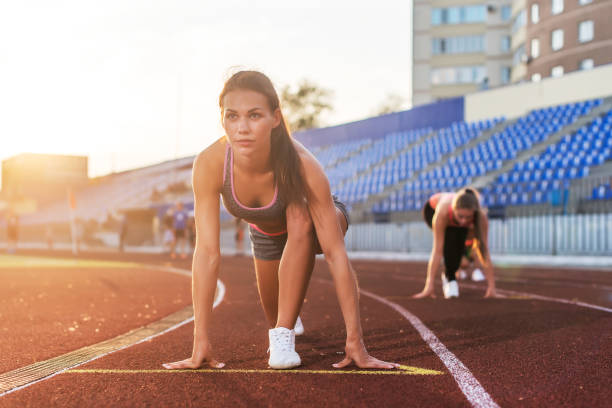 istock Women sprinters at starting position ready for race on racetrack. 953205822