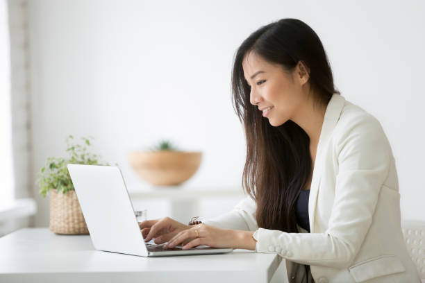 Smiling young asian businesswoman using computer working online on laptop