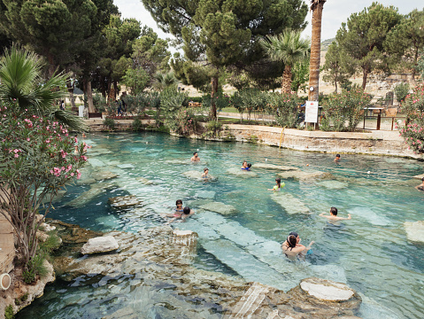 Pamukkale ,Denizli , TURKEY - April 29 2018: People are bathing at thermal Cleopatra's Pool  in Hierapolis in Pamukkale Cotton Castle. Pool is also  called antique pool.There are ancient structures inside pool.So the view of pool is spectacular.Pamukkale is one of the UNESCO World Heritage Site in Turkey.