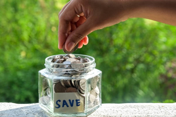 istock Close-Up Of Human Hand Holding Coins Over Jar With Save Label On Retaining Wall 953230556