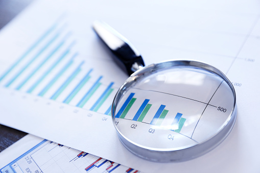 A magnifying glass rests on top of a bar graph that shows declining sales or performance over a quarterly basis.  The image is photographed using a very shallow depth of field.