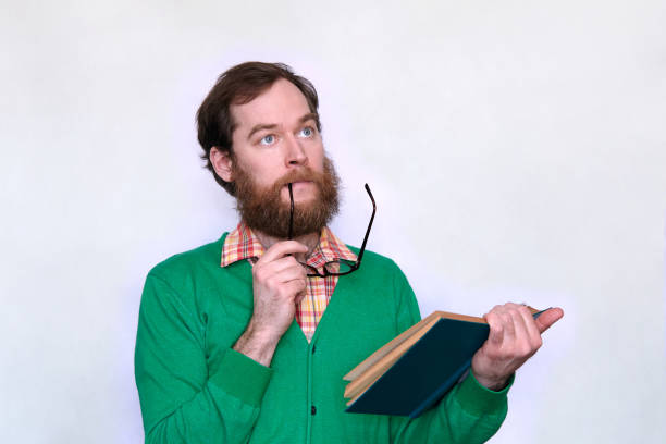 istock Pensive man looking up with book in one hand and eyeglasses in another 953247370