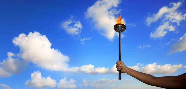 istock hand holding burning flaming torch with flames over cloudy blue sky 953251304