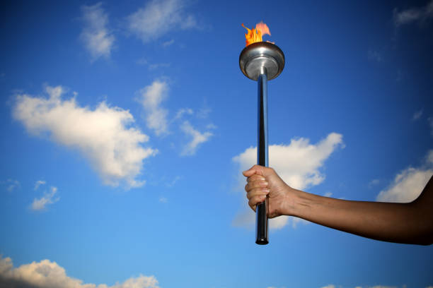 istock hand holding burning flaming torch with flames over cloudy blue sky 953251376