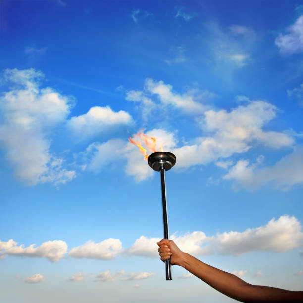 istock hand holding burning flaming torch with flames over cloudy blue sky 953251542