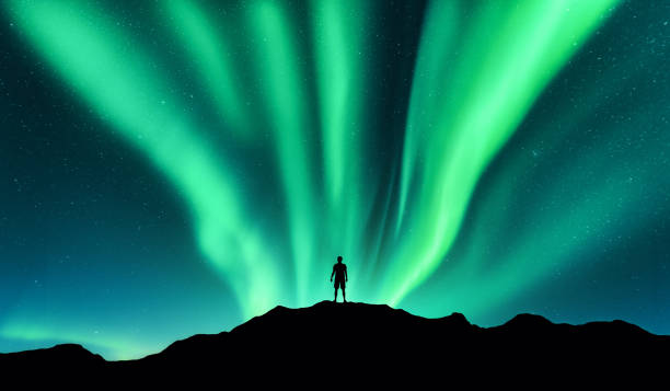 オーロラと立っている人のシルエット。ロフォーテン諸島、ノルウェー。オーロラと幸せな男。星と緑の極のライトが付いている空。オーロラと人々 の夜の風景です。コンセプトです。自然 - aurora borealis iceland aurora polaris astronomy ストックフォトと画像