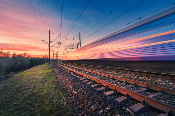 train à grande vitesse passagers en mouvement sur le chemin de fer au coucher du soleil. train de banlieue moderne floue. gare et ciel coloré. voyage en chemin de fer, tourisme ferroviaire. paysage industriel. transport - railroad track railroad station platform transportation freight transportation photos et images de collection