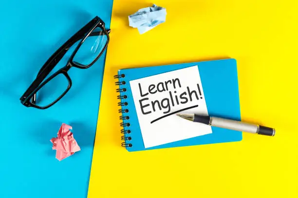 Photo of Learn english - note at blue and yellow background with teachers glasses
