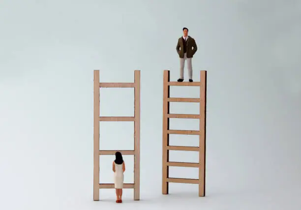 Photo of Wooden ladders and miniature people. The concept of gender inequality in promotion.
