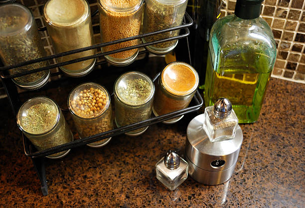 Close-up of rack full of spices with salt and olive oil A rack of spices sits next to a half empty bottle of olive oil with a small salt and pepper shaker with a stainless steel timer in the foreground. Set against brown marble mosaic tiles and brown granite countertops. spice rack stock pictures, royalty-free photos & images