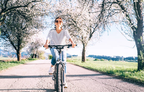 glücklich lächelnde frau reitet ein fahrrad auf der landstraße unter blühenden bäumen - apple blossom single flower spring blossom stock-fotos und bilder