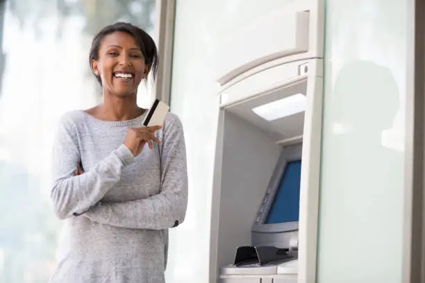 Portrait of happy debit / credit cardholder woman using a payment card to withdraw cash money from an ATM machine.