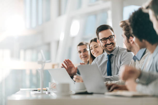 Happy businessman talking to his colleagues on a meeting in the office, Young happy entrepreneur talking to his colleagues during a business meeting in a board room. team meeting stock pictures, royalty-free photos & images