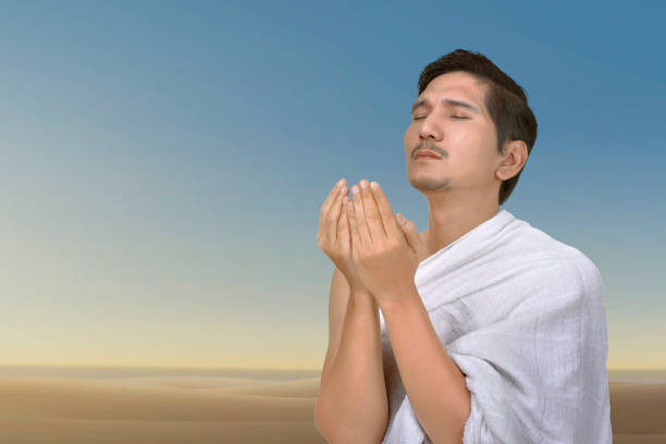 Young asian muslim man praying to god over blue sky background