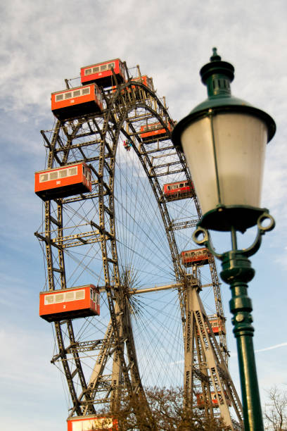 viena prater parque de diversões gigante roda com cabines vermelhas. foto tirada do chão com um poste de luz turva - ferris wheel carnival wheel amusement park ride - fotografias e filmes do acervo