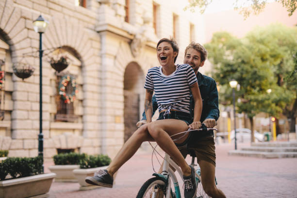 paseo en pareja disfrutando de una bicicleta en la ciudad - couple young women cheerful outdoors fotografías e imágenes de stock