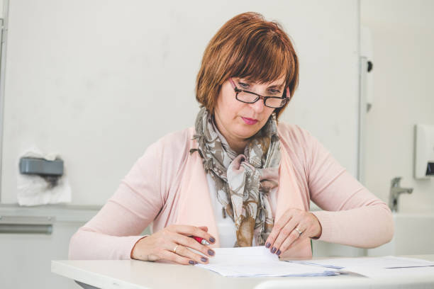 Mature Female Chemistry Teacher Correcting Test Papers in a High School Classroom, Europe Mature female chemistry teacher correcting test papers in a high school classroom, Primorska, Slovenia, Europe. Nikon D850. nova gorica stock pictures, royalty-free photos & images