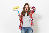 Young crazy loony woman in casual clothes holding paint roller for wall painting and clinging to head isolated on white background. Instruments for renovation apartment room. Repair home concept.