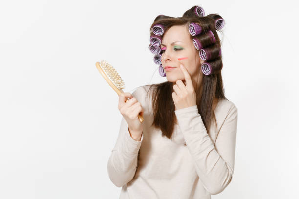 istock Young woman with curlers using combing with comb her hair isolated on white background. Crazy makeup with set facial decorative cosmetics. Beauty female fashion lifestyle concept. Area to copy space. 953441818